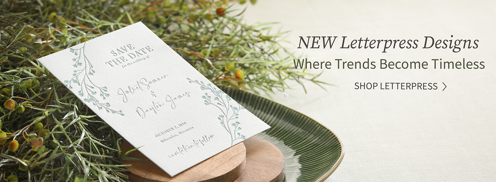 A letterpress save the date with greenery design is shown laying against fresh greenery.
